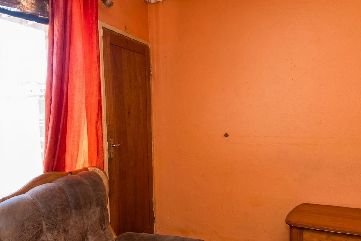 A bedroom interior featuring orange painted walls, a wooden door, and coving, showing signs of wear and a small hole in the wall.