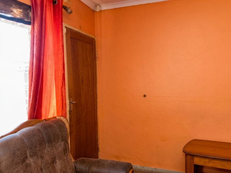 A bedroom interior featuring orange painted walls, a wooden door, and coving, showing signs of wear and a small hole in the wall.