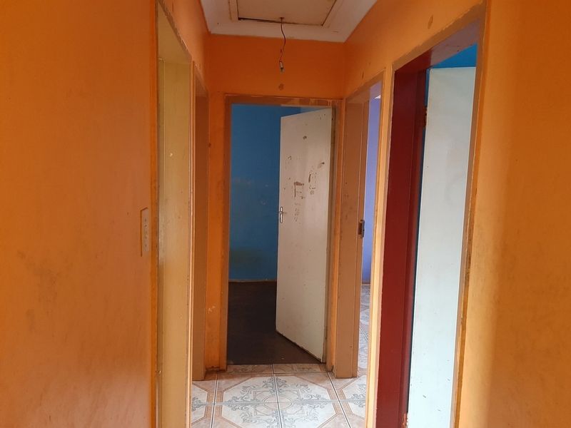 A narrow hallway featuring tiled flooring and multiple doorways leading to adjacent rooms, showing signs of wear and requiring cosmetic updates.