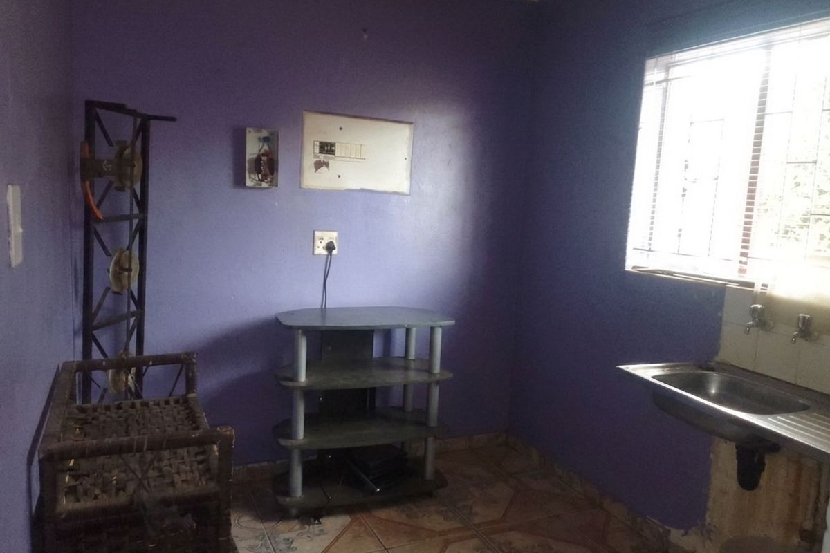 A small kitchen area featuring a stainless steel sink, tiled flooring, and an exposed electrical distribution board, requiring cosmetic updates and repairs.