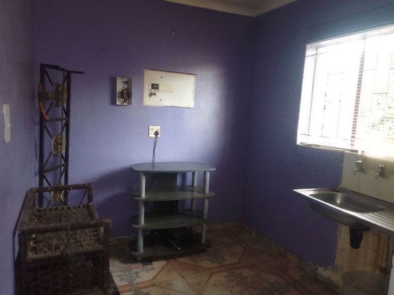 A small kitchen area featuring a stainless steel sink, tiled flooring, and an exposed electrical distribution board, requiring cosmetic updates and repairs.