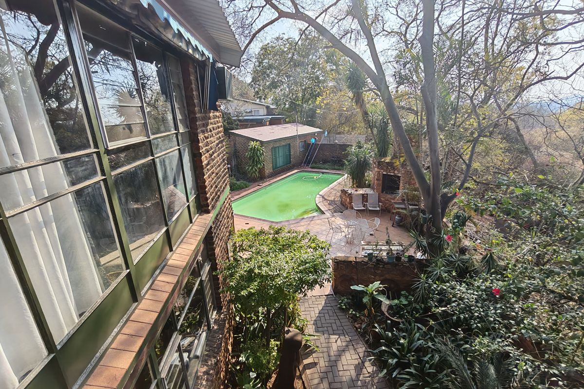 Rear exterior view featuring a swimming pool, paved patio area with built-in braai, and established garden surroundings.