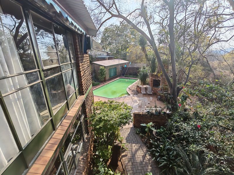 Rear exterior view featuring a swimming pool, paved patio area with built-in braai, and established garden surroundings.