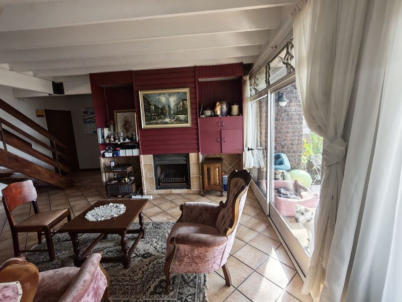 Living room featuring a fireplace with built-in cabinetry, exposed beam ceiling, tiled flooring, and large sliding glass doors providing access to the patio.