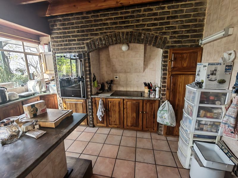 A rustic kitchen featuring exposed brickwork, timber cabinetry, tiled flooring, and built-in cooking appliances, offering a warm and traditional aesthetic.