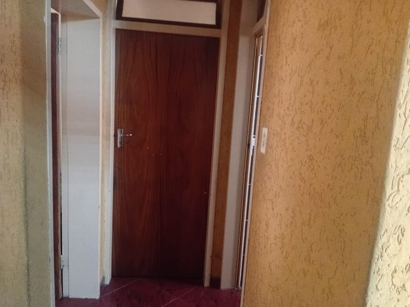A narrow hallway featuring textured walls, tiled flooring, and a wooden door with a transom window above.