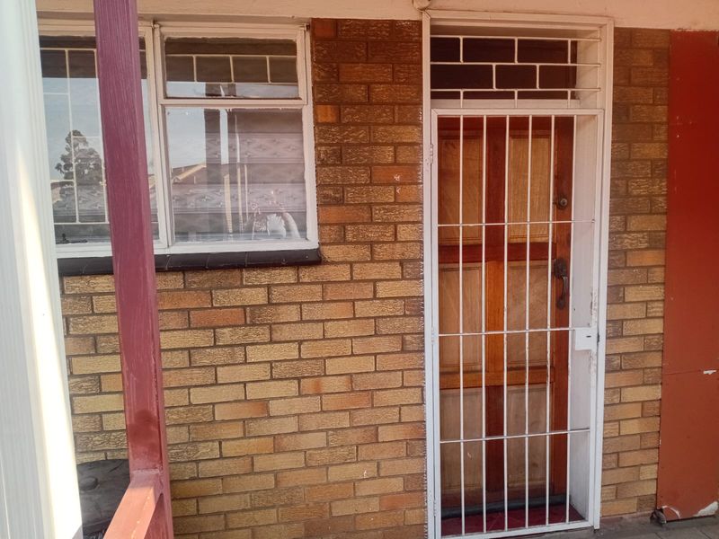 Front entrance of the flat featuring a timber door with a white security gate and brick facade.