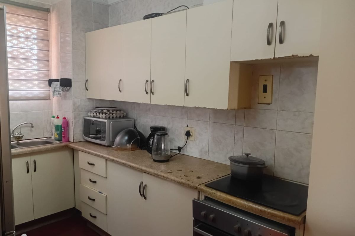 A compact kitchen featuring dated built-in cabinetry, laminate countertops, tiled splashbacks, and a built-in electric stove with oven.
