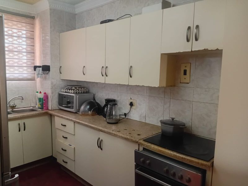 A compact kitchen featuring dated built-in cabinetry, laminate countertops, tiled splashbacks, and a built-in electric stove with oven.