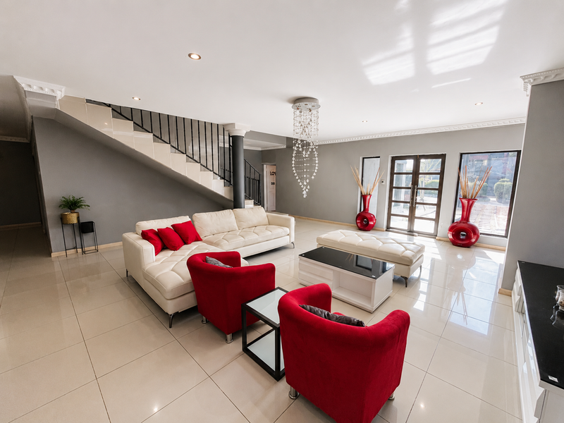 Spacious open-plan living area featuring polished porcelain tiles, a modern staircase with wrought iron balustrade, and elegant crystal chandelier lighting.