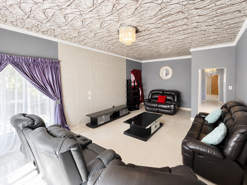 Spacious living room featuring large format floor tiles, a textured ceiling finish, and a neutral tiled feature wall.