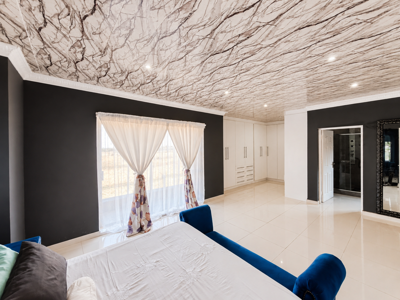 Spacious bedroom featuring modern dark accent walls, a unique marble-effect ceiling, built-in cabinetry, and large sliding doors leading to the exterior.