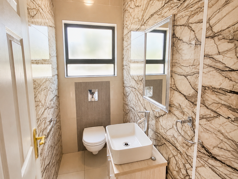 A modern guest bathroom featuring marble-effect wall tiling, a wall-mounted toilet, and a contemporary vessel sink vanity unit.