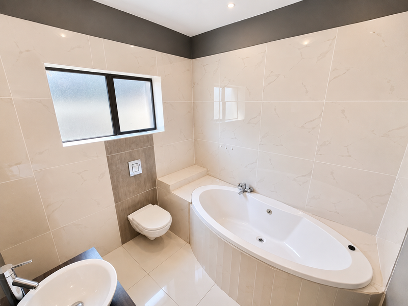 Modern bathroom featuring a built-in bathtub, wall-mounted toilet with concealed cistern, and neutral marble-look wall tiles.