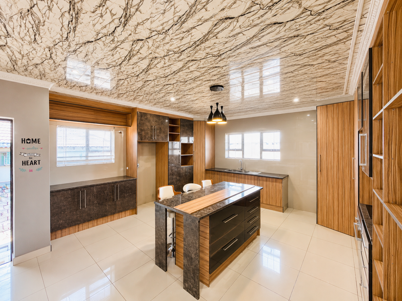 Modern kitchen featuring a central island, extensive built-in cabinetry, high-gloss porcelain flooring, and a distinctive marble-patterned ceiling finish.