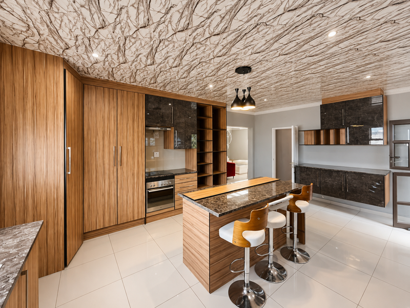 Modern kitchen featuring wood-grain and dark marble-finish cabinetry, a central island with breakfast bar, built-in appliances, and a distinctive marble-patterned ceiling.