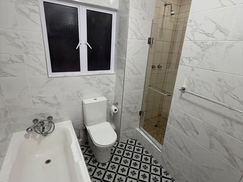 A modern bathroom featuring marble-look wall tiles, patterned floor tiles, a bathtub, and a separate glass-enclosed shower.
