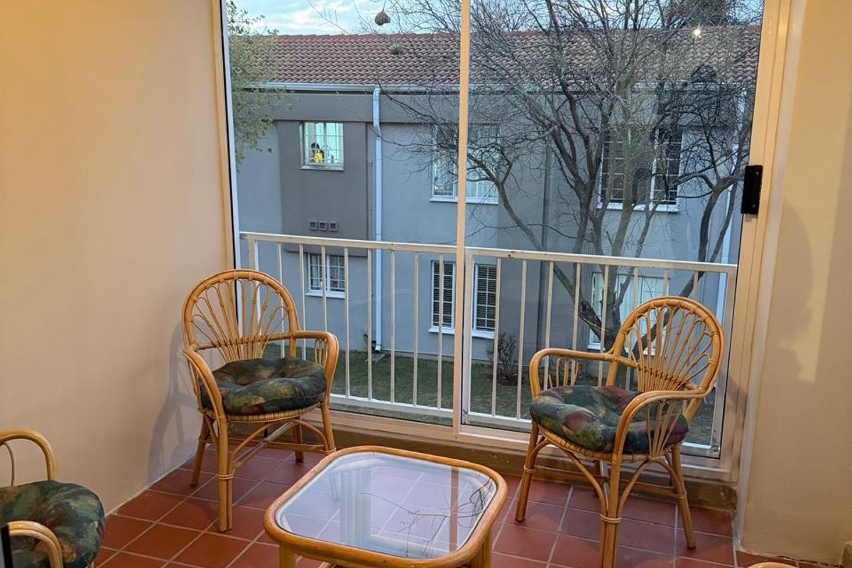 A covered balcony featuring tiled flooring, a large sliding glass door, and a metal balustrade overlooking the complex grounds.