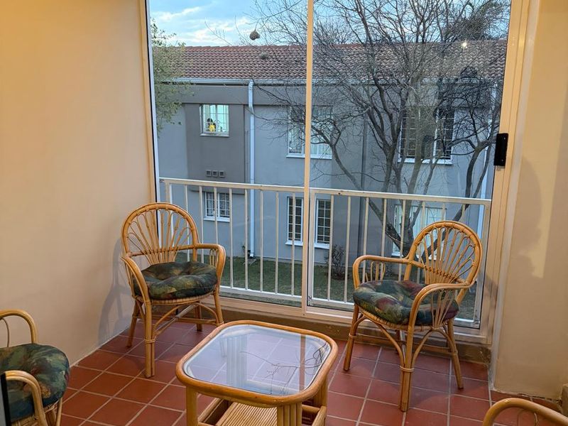 A covered balcony featuring tiled flooring, a large sliding glass door, and a metal balustrade overlooking the complex grounds.
