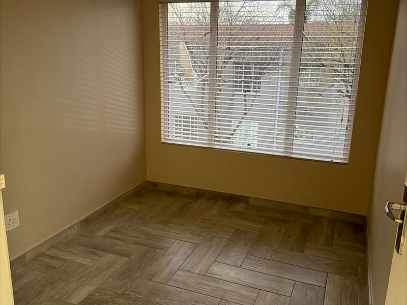 A bright, empty bedroom featuring modern herringbone wood-look tile flooring and fitted venetian blinds, offering a clean and neutral space ready for furnishing.