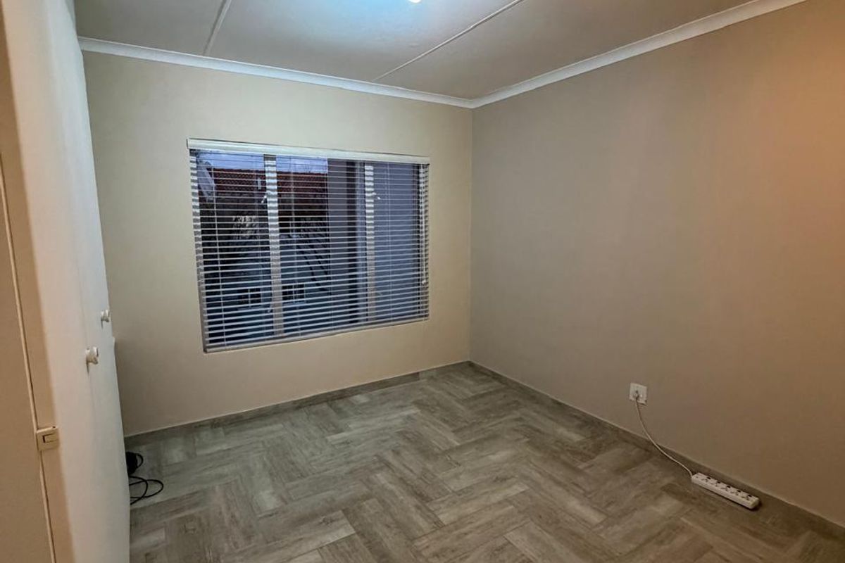 A clean, empty bedroom featuring modern herringbone tile flooring, a built-in cupboard, and neutral wall tones, ready for personalization.
