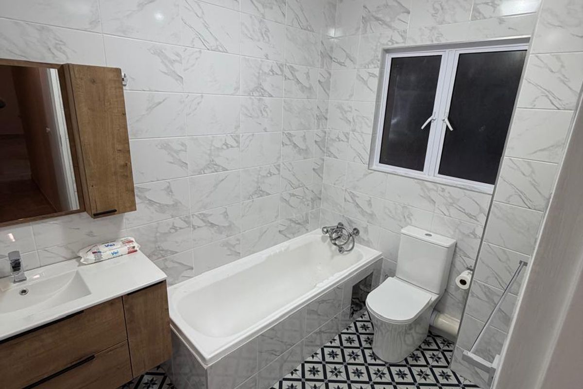 A modern bathroom featuring marble-look wall tiles, patterned floor tiles, a vanity unit with basin, and a bathtub with shower mixer.