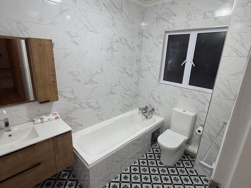 A modern bathroom featuring marble-look wall tiles, patterned floor tiles, a vanity unit with basin, and a bathtub with shower mixer.