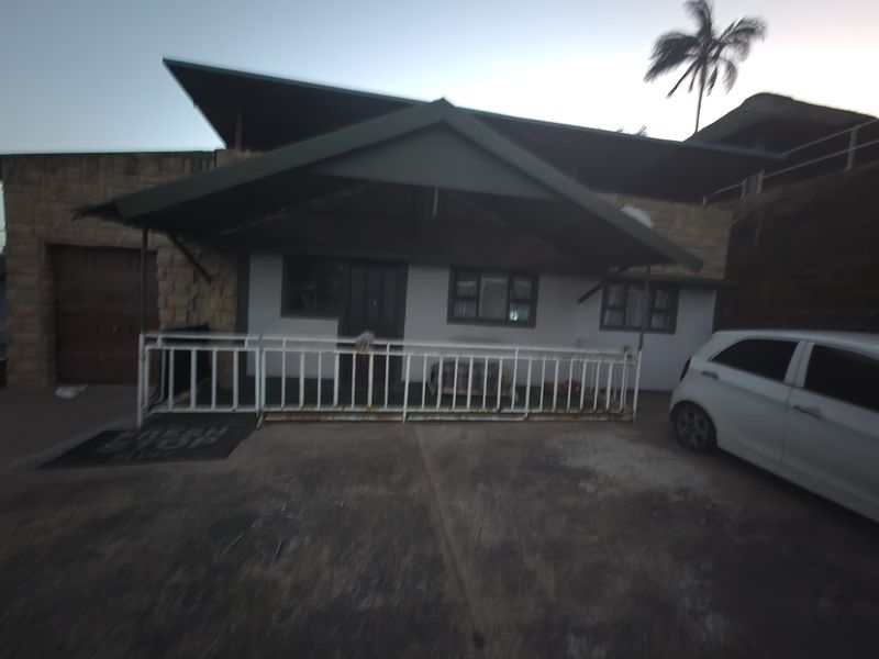 Front exterior view of the apartment building featuring a covered entrance, stone cladding, and a concrete driveway with metal security railing.