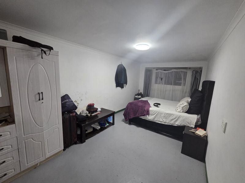 A bedroom featuring a window, ceiling cornice, and flush mount lighting. The walls show visible signs of staining and surface wear.