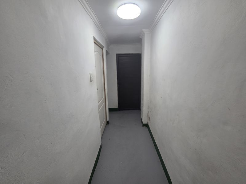 A narrow interior hallway featuring painted walls, skirting boards, and a ceiling light fixture, showing signs of wear and surface imperfections.