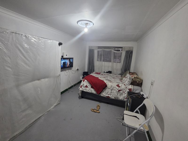 A bedroom featuring a window, cove cornicing, and electrical points. The room requires cosmetic updates to the flooring and general finishes.