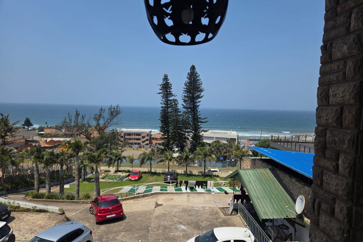 Elevated coastal view overlooking a residential area, parking space, and the ocean horizon from a balcony with stone-clad pillars.