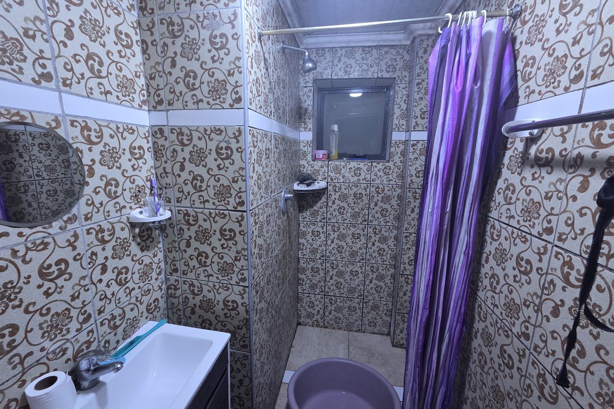 A compact bathroom featuring dated patterned wall tiles, a vanity basin with mixer tap, and a shower area with a curtain rail.