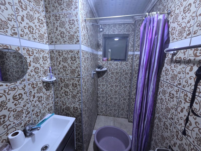 A compact bathroom featuring dated patterned wall tiles, a vanity basin with mixer tap, and a shower area with a curtain rail.