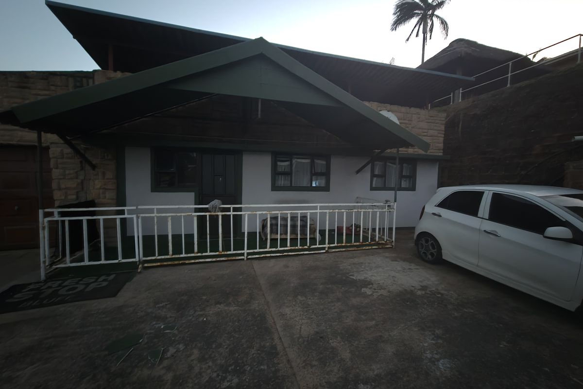 Front exterior view of the apartment featuring a covered entrance, stone cladding, and a concrete driveway with a metal security railing.