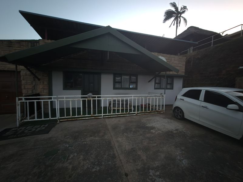 Front exterior view of the apartment featuring a covered entrance, stone cladding, and a concrete driveway with a metal security railing.