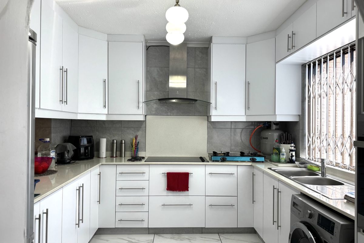 Modern U-shaped kitchen featuring white cabinetry, stone countertops, dual hobs, stainless steel extractor fan, and integrated laundry plumbing under a double sink.