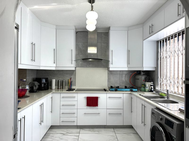 Modern U-shaped kitchen featuring white cabinetry, stone countertops, dual hobs, stainless steel extractor fan, and integrated laundry plumbing under a double sink.