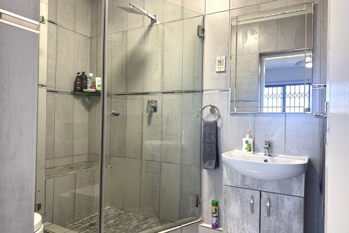 Modern bathroom featuring a glass-enclosed shower with a rain shower head, tiled finishes, and a wall-mounted vanity with a ceramic basin.