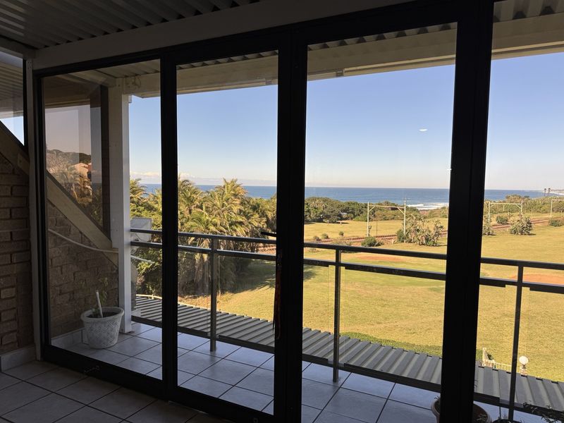 A covered balcony featuring tiled flooring, a modern glass balustrade, and sliding doors, offering expansive views of the surrounding landscape and coastline.