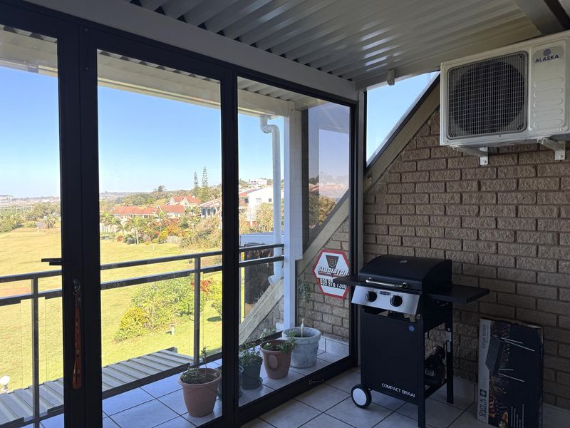 A covered balcony featuring tiled flooring, exposed brickwork, an air conditioning unit, and sliding glass doors with scenic views.