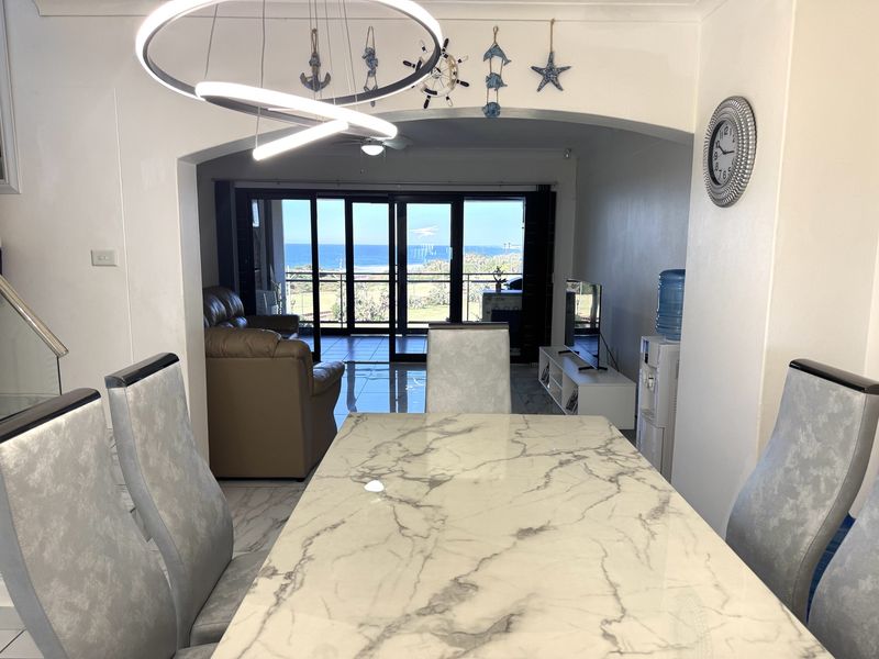Open plan dining and living area featuring tiled floors, a modern pendant light, and large sliding glass doors leading to a balcony with ocean views.