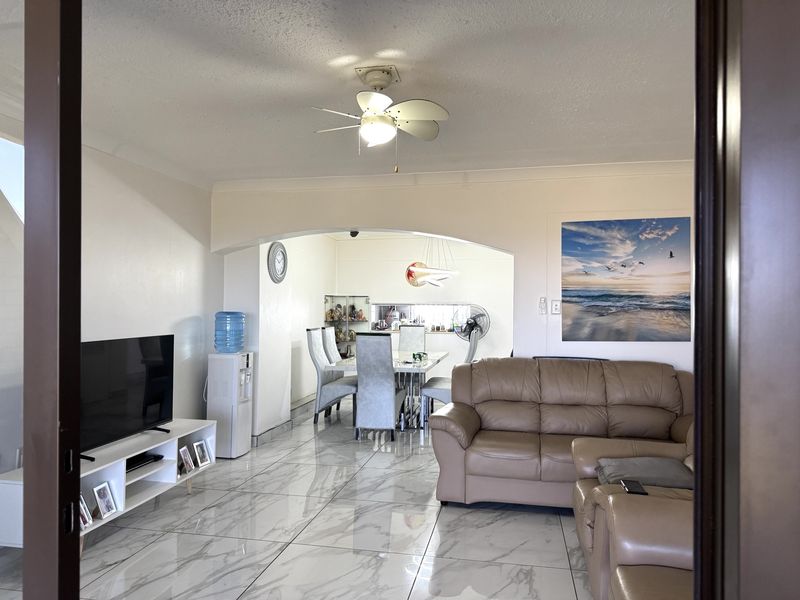 Open-plan living and dining area featuring marble-look floor tiles, a central ceiling fan, and a decorative archway connecting the two spaces.