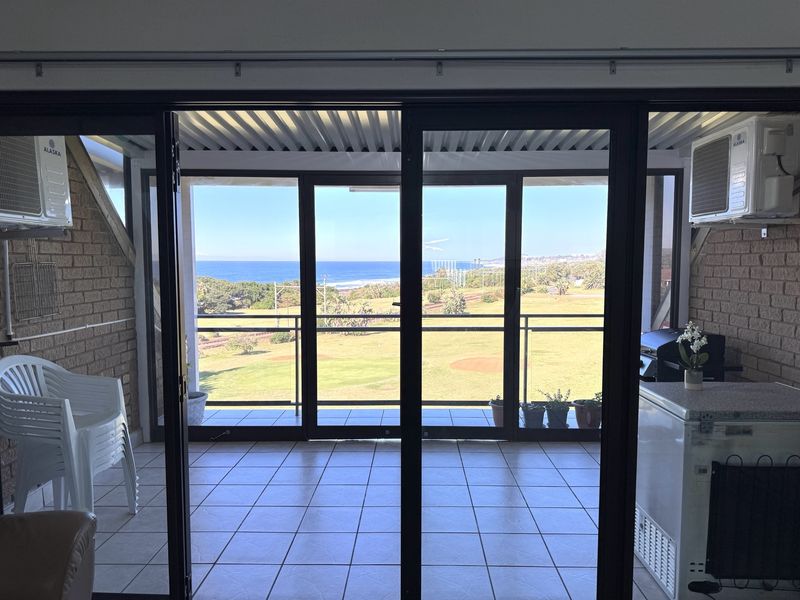 A covered balcony featuring tiled floors, exposed brick walls, and sliding glass doors that offer expansive ocean and coastal views.