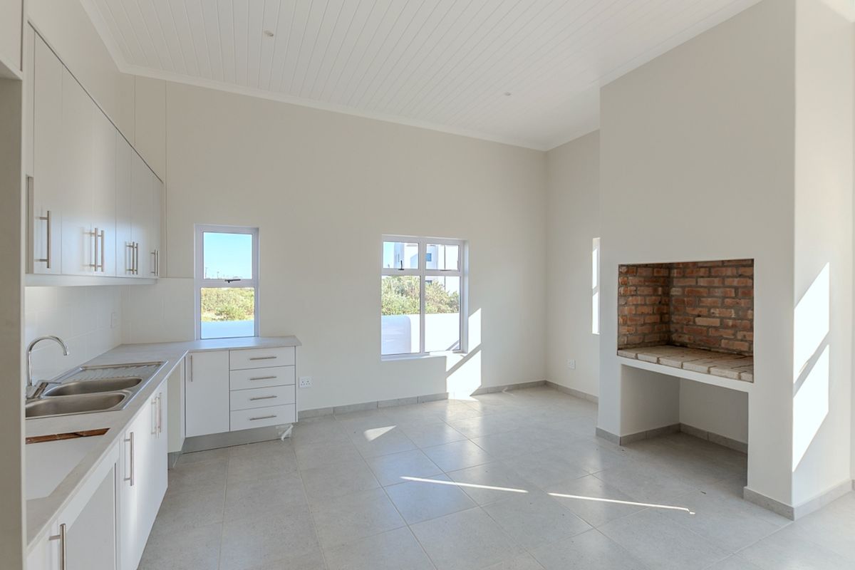 Bright open-plan living area featuring a modern kitchen with built-in cabinetry, tiled floors, and a rustic exposed brick fireplace.
