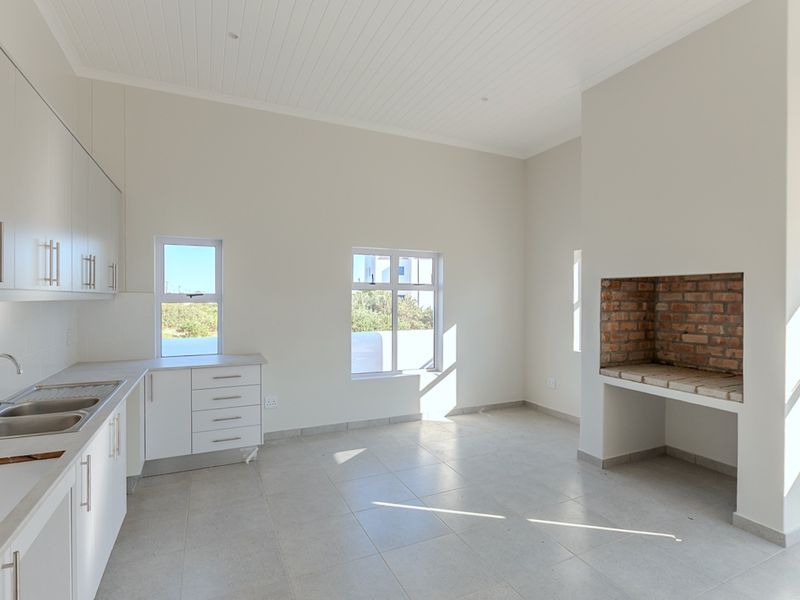 Bright open-plan living area featuring a modern kitchen with built-in cabinetry, tiled floors, and a rustic exposed brick fireplace.
