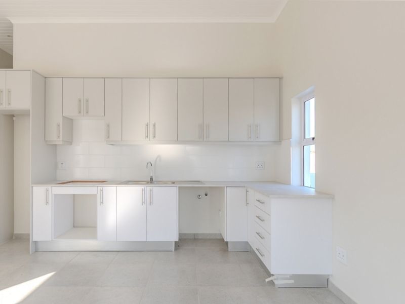 A clean, modern, and empty kitchen featuring white cabinetry, tiled backsplash, and neutral floor tiles, ready for appliance installation.
