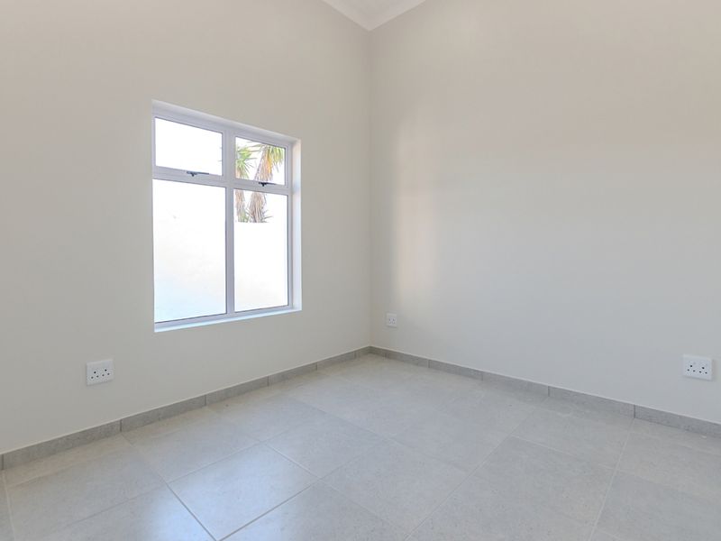 A clean, empty bedroom featuring neutral tiled flooring, white walls, and a built-in cupboard, offering a blank canvas for personalization.
