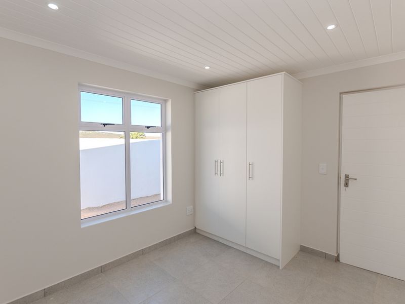 A clean, modern bedroom featuring neutral tiled floors, a built-in wardrobe, and a white tongue and groove ceiling with recessed lighting.