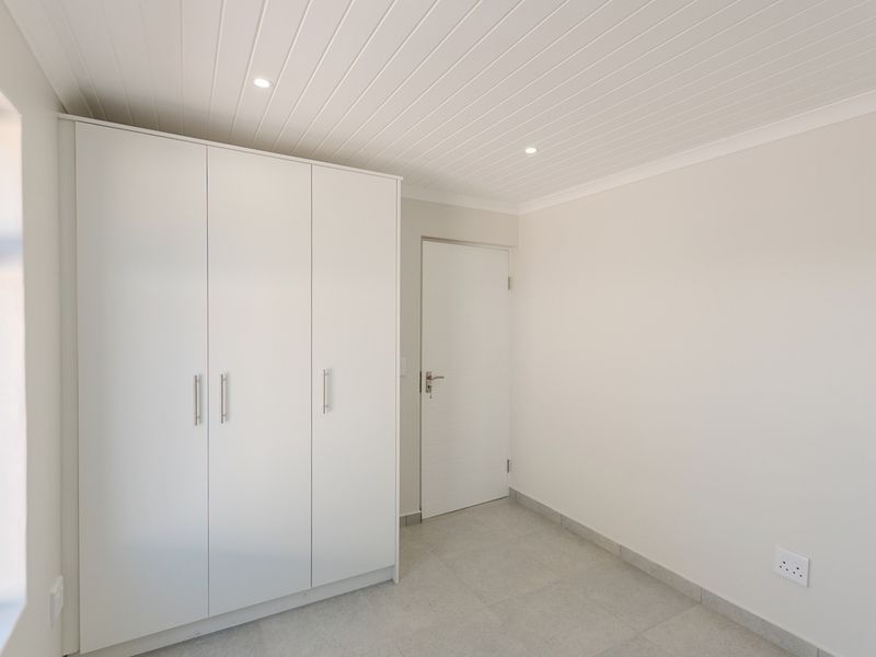 A clean, modern bedroom featuring built-in cupboards, tiled flooring, and a neat tongue and groove ceiling with recessed lighting.